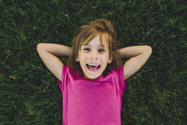 Overhead-Porträt eines fröhlichen Mädchens mit den Händen hinter dem Kopf, das auf einer Wiese liegt - CAVF10518