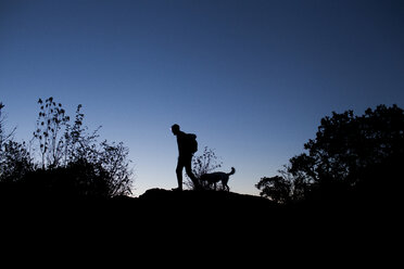 Silhouette man walking with dog on field against clear blue sky - CAVF10533