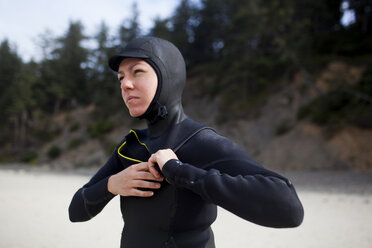 Woman wearing wetsuit while standing at beach - CAVF10544