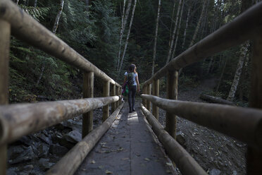 Rückansicht einer Frau, die auf einer Holzbrücke im Wald geht - CAVF10549