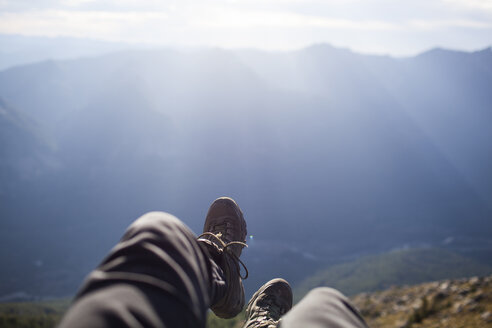 Niedriger Ausschnitt eines Wanderers, der auf einer Klippe vor den Bergen sitzt - CAVF10559