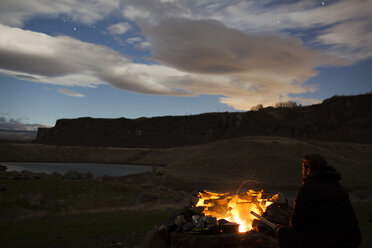 Hiker sitting by campfire against cloudy sky - CAVF10582