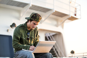 Niedriger Blickwinkel eines Mannes, der einen Laptop-Computer benutzt, während er in einem Schiff sitzt - CAVF10604