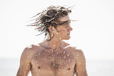 Mann spritzt Wasser aus nassen Haaren gegen klaren Himmel - CAVF10610