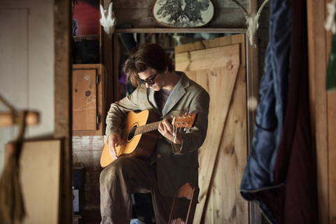 Mann spielt Akustikgitarre, während er zu Hause steht, lizenzfreies Stockfoto