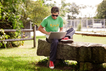 Mann benutzt Laptop, während er auf einem Felsen im Park sitzt - CAVF10646