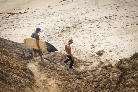 Mann trägt Surfbrett beim Spaziergang mit Freund am Strand, lizenzfreies Stockfoto