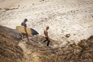 Mann trägt Surfbrett beim Spaziergang mit Freund am Strand - CAVF10661