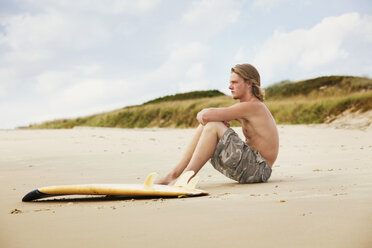Mann mit Surfbrett auf Sand am Strand sitzend - CAVF10667