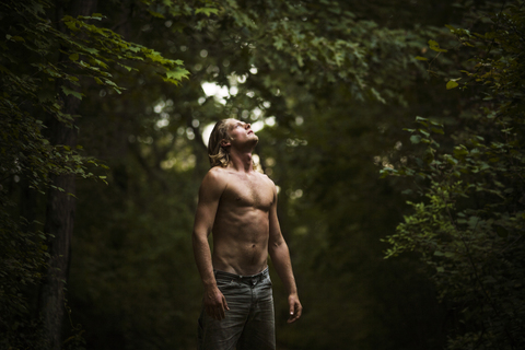 Mann ohne Hemd schaut im Wald stehend nach oben, lizenzfreies Stockfoto