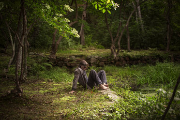 Mann sitzt auf einem Feld im Wald - CAVF10691