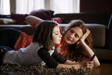 Mother and daughter lying on rug at home - CAVF10720