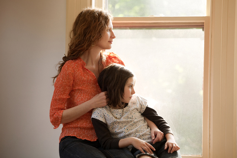 Mutter und Tochter schauen durch das Fenster, während sie zu Hause sitzen, lizenzfreies Stockfoto