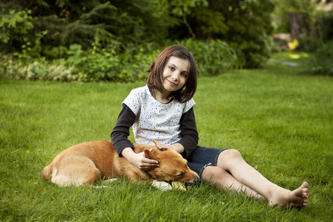 Porträt eines Mädchens, das mit einem Hund auf einer Wiese im Hof sitzt, lizenzfreies Stockfoto