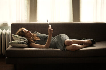 Frau in voller Länge bei der Benutzung eines Tablet-Computers, während sie zu Hause auf dem Sofa liegt - CAVF10738