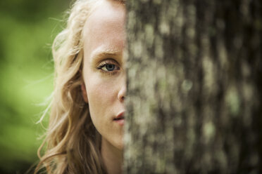 Portrait of woman standing behind tree - CAVF10752