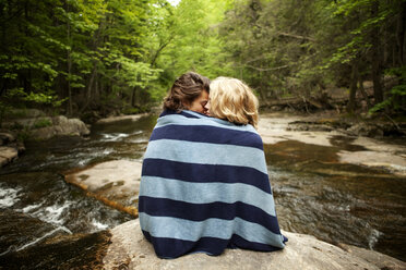 In Handtuch eingewickeltes Paar sitzt auf Felsen im Fluss - CAVF10760