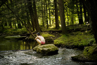 Rear view of girl sitting on rock in river - CAVF10783