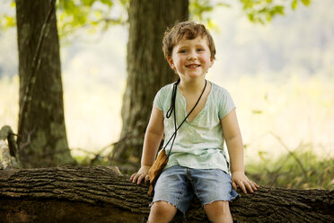 Porträt eines süßen Jungen, der auf einem umgefallenen Baumstamm sitzt - CAVF10791