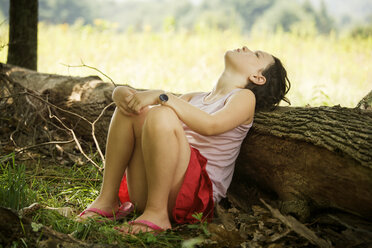 Mädchen lehnt den Kopf an einen umgestürzten Baumstamm, während sie auf einem Feld sitzt - CAVF10792