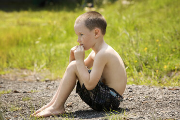 Seitenansicht eines auf einem Feld sitzenden Jungen - CAVF10793