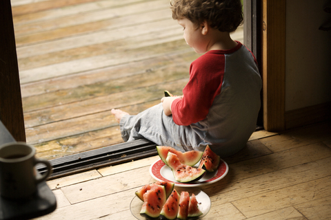 Junge sitzt in der Tür bei Wassermelonen in Tellern, lizenzfreies Stockfoto