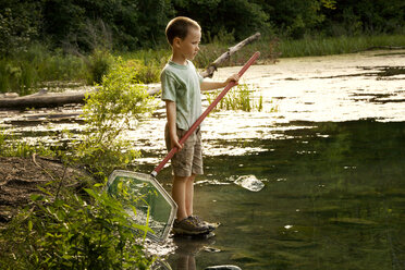 Boy holding cleaning net while standing by lake - CAVF10799