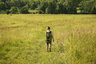 Rear view of boy with backpack walking on grassy field - CAVF10807