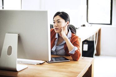 Geschäftsfrau arbeitet am Computer, während sie am Tisch im Büro sitzt - CAVF10820