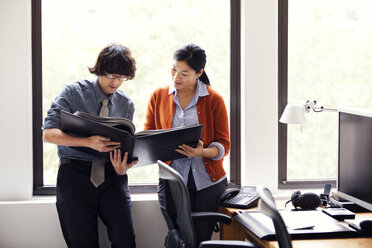 Businessman and businesswoman discussing while holding documents in office - CAVF10825