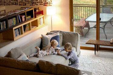 Hochformatige Ansicht von Geschwistern, die zu Hause auf dem Sofa spielen - CAVF10845
