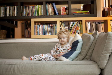 Portrait of cute boy sitting on sofa at home - CAVF10846