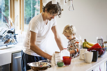 Father working while son sitting on kitchen worktop - CAVF10854