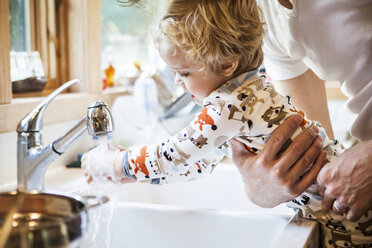 Ausgeschnittenes Bild eines Vaters, der seinen Sohn beim Händewaschen an der Küchenspüle hält - CAVF10856