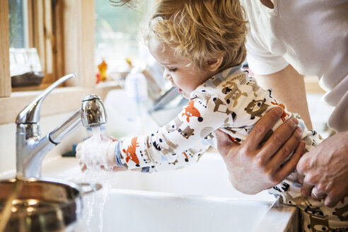 Cropped image of father holding son while washing hands at kitchen sink - CAVF10856