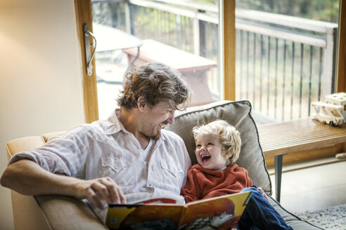 Glücklicher Vater sitzt mit seinem Sohn auf dem Sofa zu Hause - CAVF10894