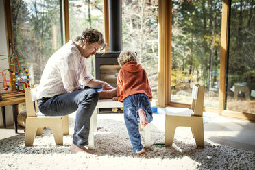 Father teaching son to write while sitting on chair at home - CAVF10901