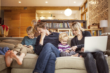 Happy family sitting on sofa at home - CAVF10931