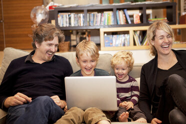 Siblings using laptop while sitting with parents on sofa at home - CAVF10933