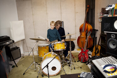 Father teaching son to play drums at home - CAVF10936