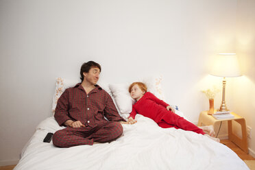 Vater und Sohn halten sich an den Händen, während sie zu Hause auf dem Bett sitzen - CAVF10944
