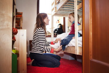 Side view of mother assisting son to wear sock at bedroom - CAVF10953