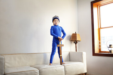 Junge im Superheldenkostüm hält ein Schwert, während er auf dem Sofa steht - CAVF10957