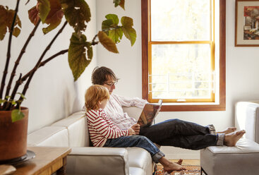 Vater und Sohn lesen ein Buch, während sie zu Hause auf dem Sofa sitzen - CAVF10962