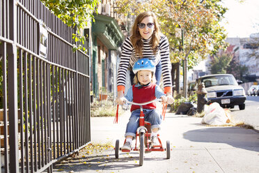 Playful mother with son cycling on footpath - CAVF10971