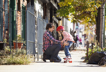 Vater hilft seinem Sohn, auf dem Skateboard zu stehen - CAVF10972