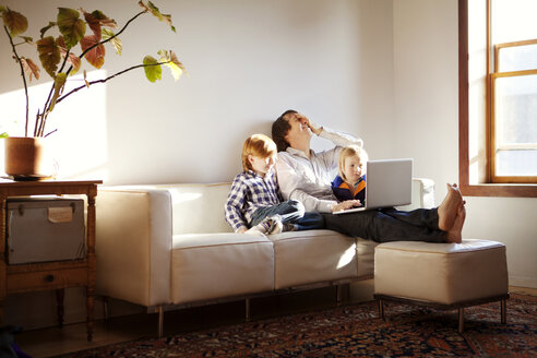 Vater benutzt Laptop, während er mit seinen Söhnen zu Hause auf dem Sofa sitzt - CAVF10989