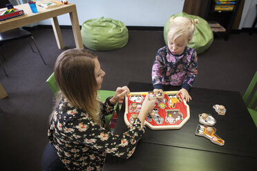 Lehrer, der einem Mädchen hilft, ein Knopfpuzzle am Tisch in der Vorschule zu spielen - CAVF11025