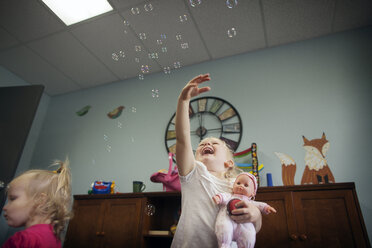 Low angle view of cheerful girl playing with bubbles at preschool - CAVF11036
