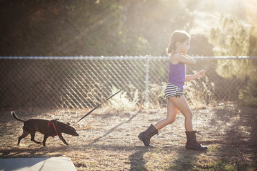 Mädchen hält die Leine eines Hundes beim Spaziergang auf einem Feld - CAVF11039